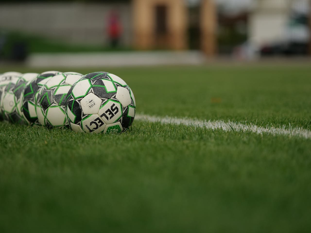 about-02 Close-up view of soccer balls lined up on a grassy football field.